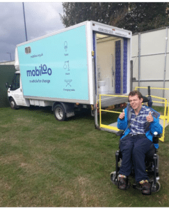 A disabled festival go-er giving Victorious two thumbs up for their accessibility infront of a Mobiloo van